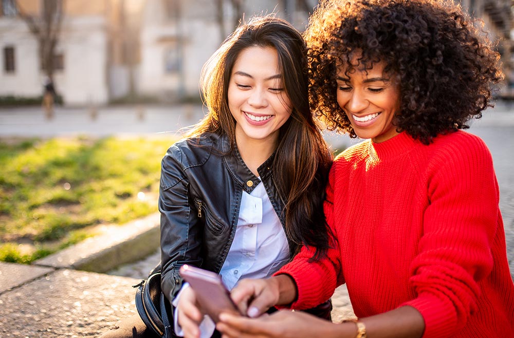 two women smiling and looking at phone